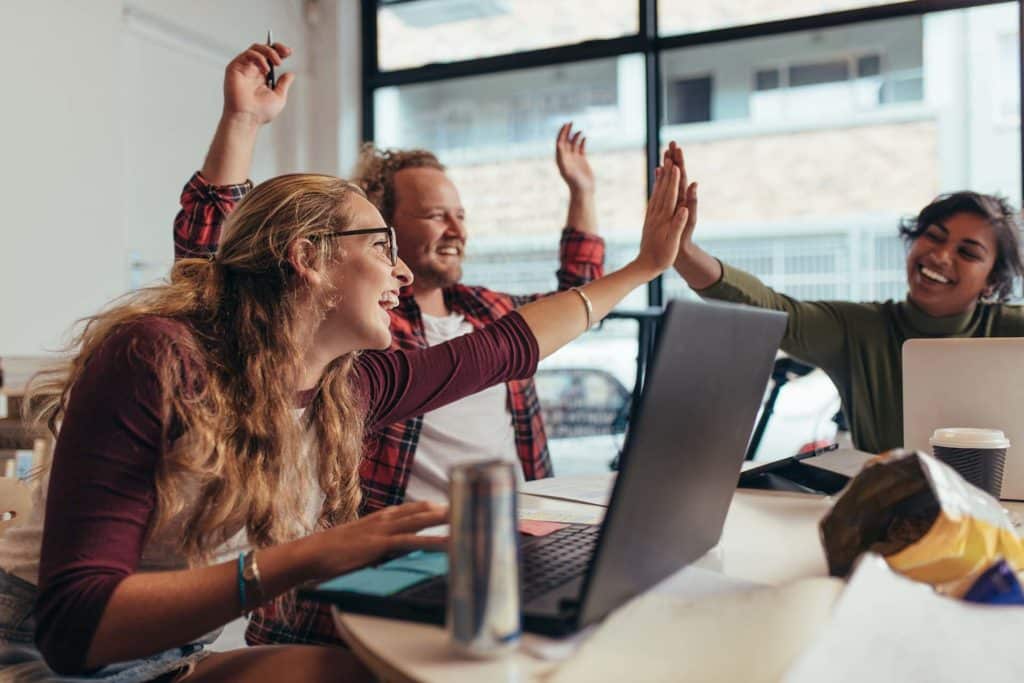 team of three people give high fives and celebrate in front of computers