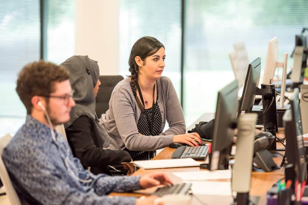 Three employees sit at desks with computers in front of them.