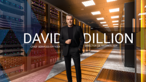 David Dillion, Chief Services Officer and Director of Technology, standing confidently in a modern, illuminated server room. He is wearing a dark suit with his hand in his pocket. A bold text overlay reads "DAVID DILLION", flanked by the titles "CHIEF SERVICES OFFICER" on the left and "DIRECTOR OF TECHNOLOGY" on the right, set against a background of glowing server racks, geometric color overlays, and an orange grated floor.